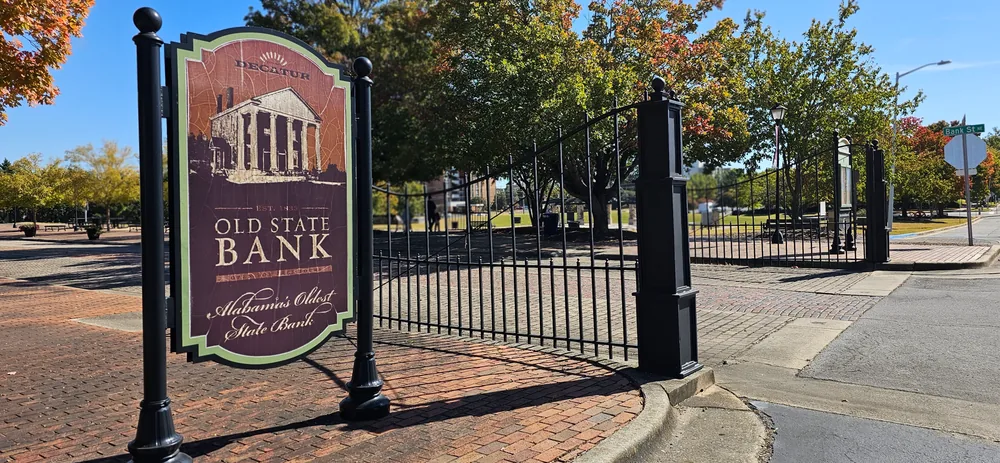 Old State Bank sign and iron gates in Decatur, with autumn trees and blue sky.